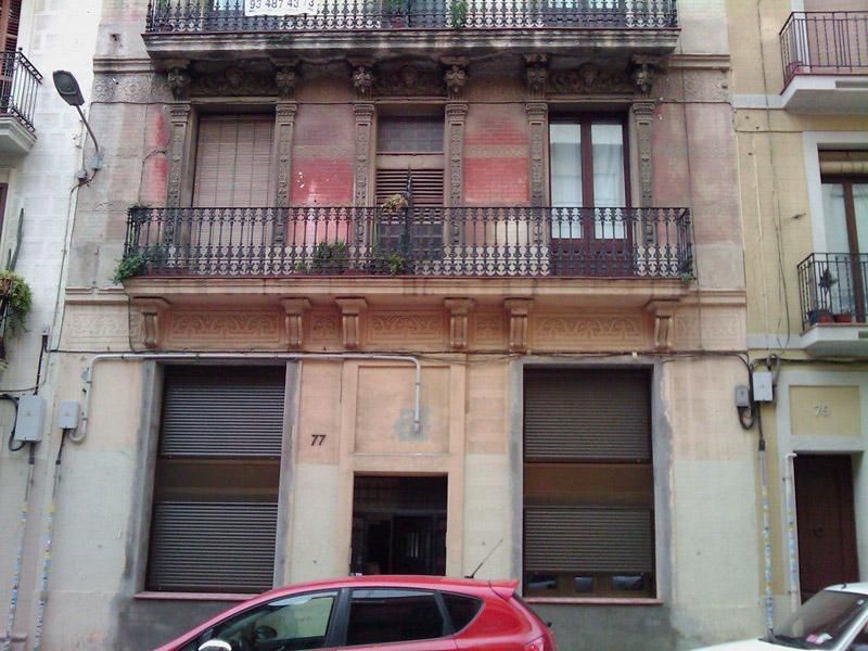 Un cotxe vermell està aparcat davant d'un edifici amb balcons