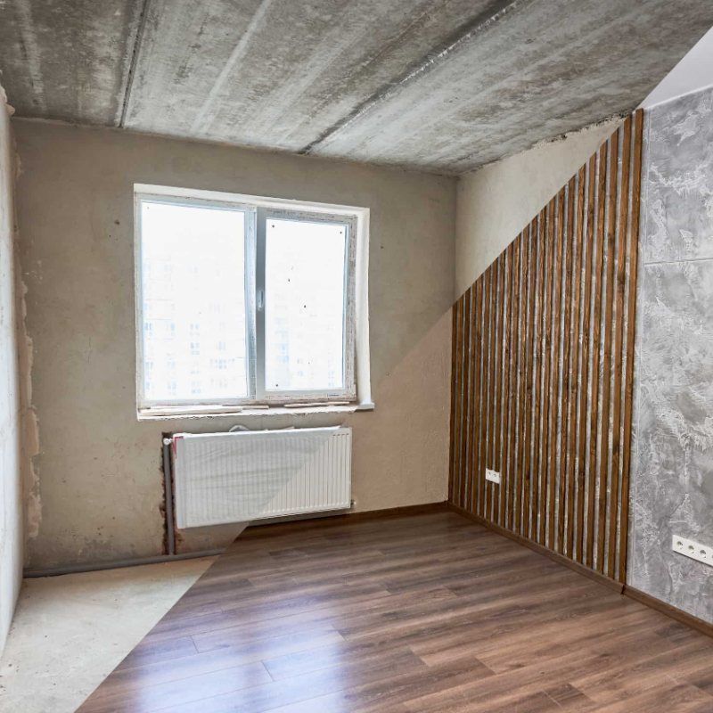 Una habitació buida amb terres de fusta, una finestra i un radiador.