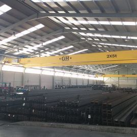 Un gran almacén lleno de vigas de acero y una grúa amarilla.