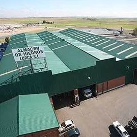 Una vista aérea de un almacén con techo verde y automóviles estacionados frente a él.