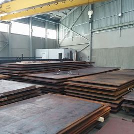 Un almacén lleno de pilas de placas de metal bajo una grúa.