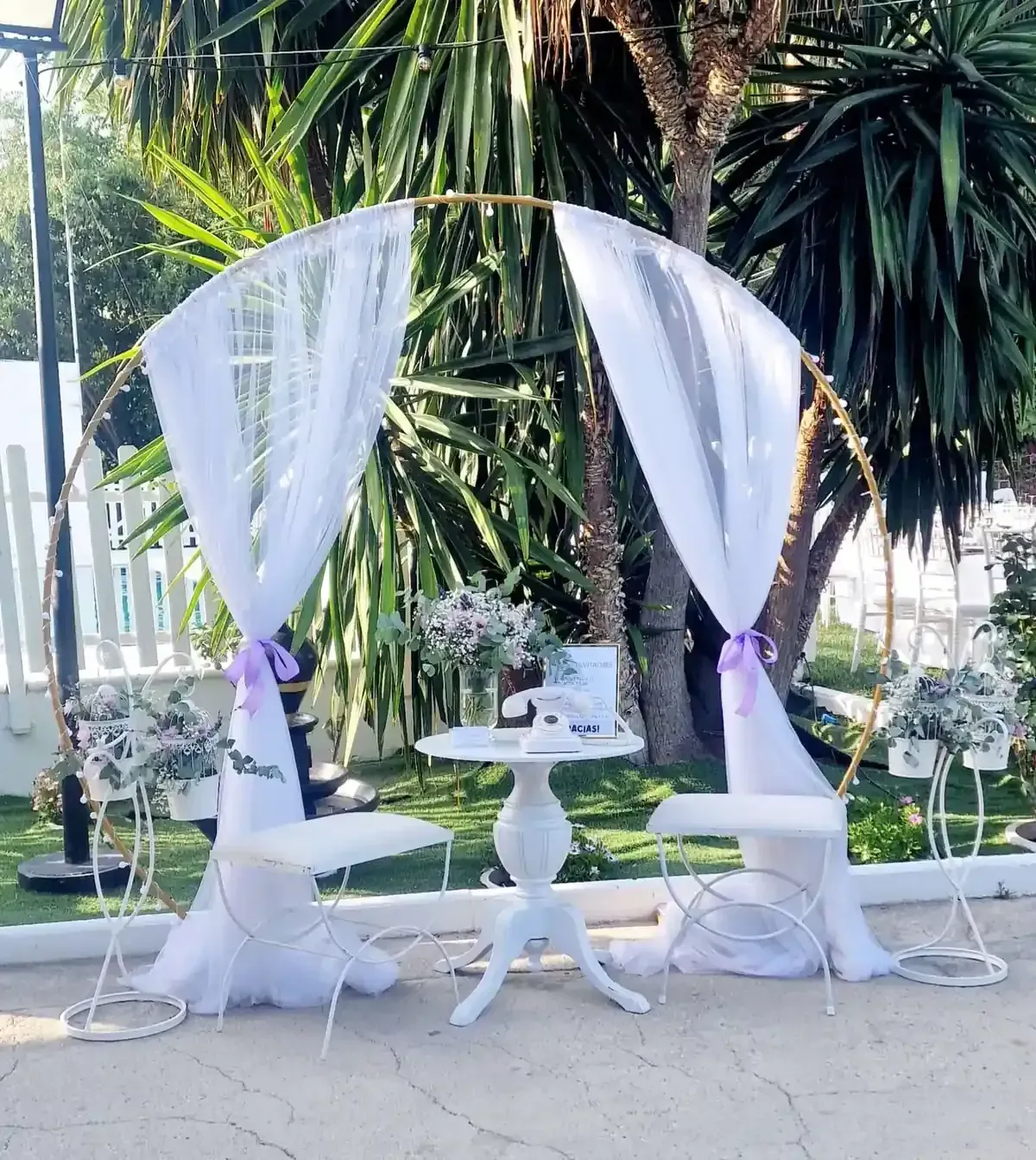 Dosel nupcial blanco con mesas y decoración floral en un entorno de jardín tropical.