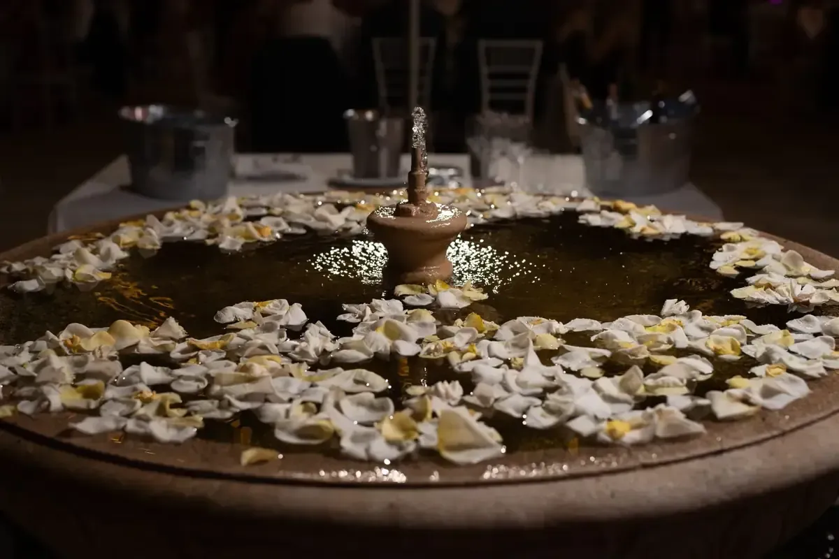 Mesa redonda de madera con pétalos de flores blancas y pequeñas velas en una habitación con poca luz.