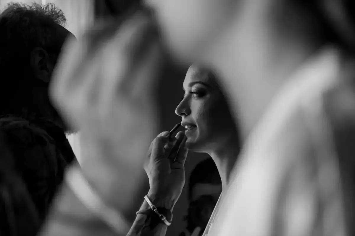 Mujer de perfil aplicándose lápiz labial en una escena borrosa en blanco y negro entre bastidores.