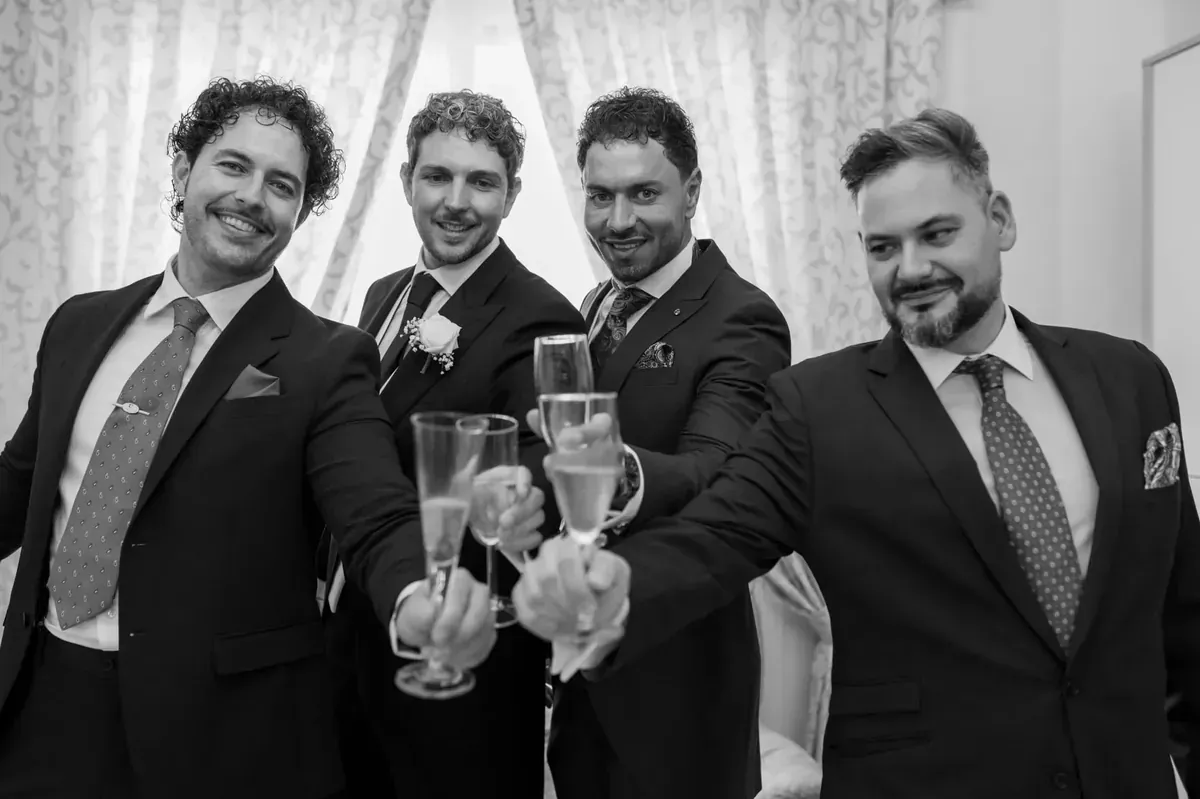 Cuatro hombres de traje sonriendo y brindando con copas de champán en un evento formal.