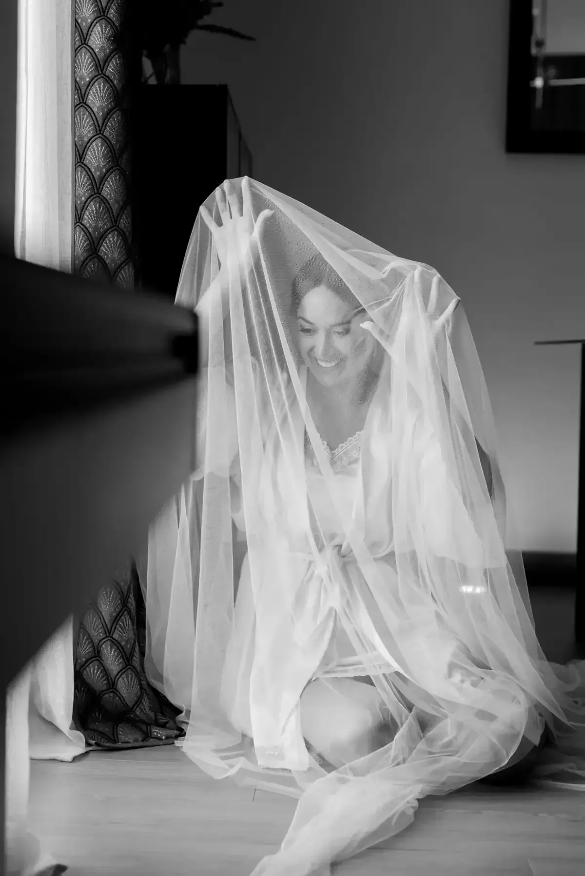 Mujer sentada en el suelo bajo un velo blanco transparente, en una escena interior en blanco y negro.