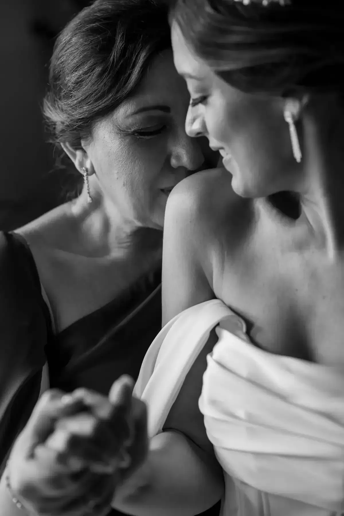En un retrato en blanco y negro, dos mujeres con vestidos de gala se inclinan muy cerca, una susurrándole algo a la otra.