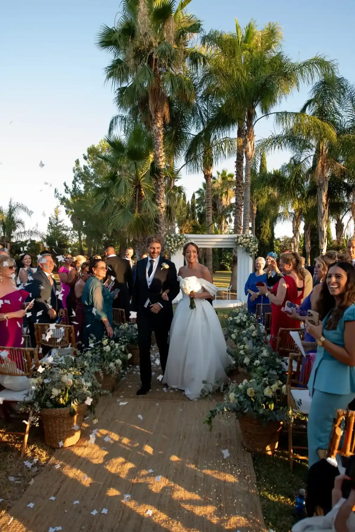 La pareja de recién casados ​​bajo un arco floral en una ceremonia al aire libre rodeada de palmeras