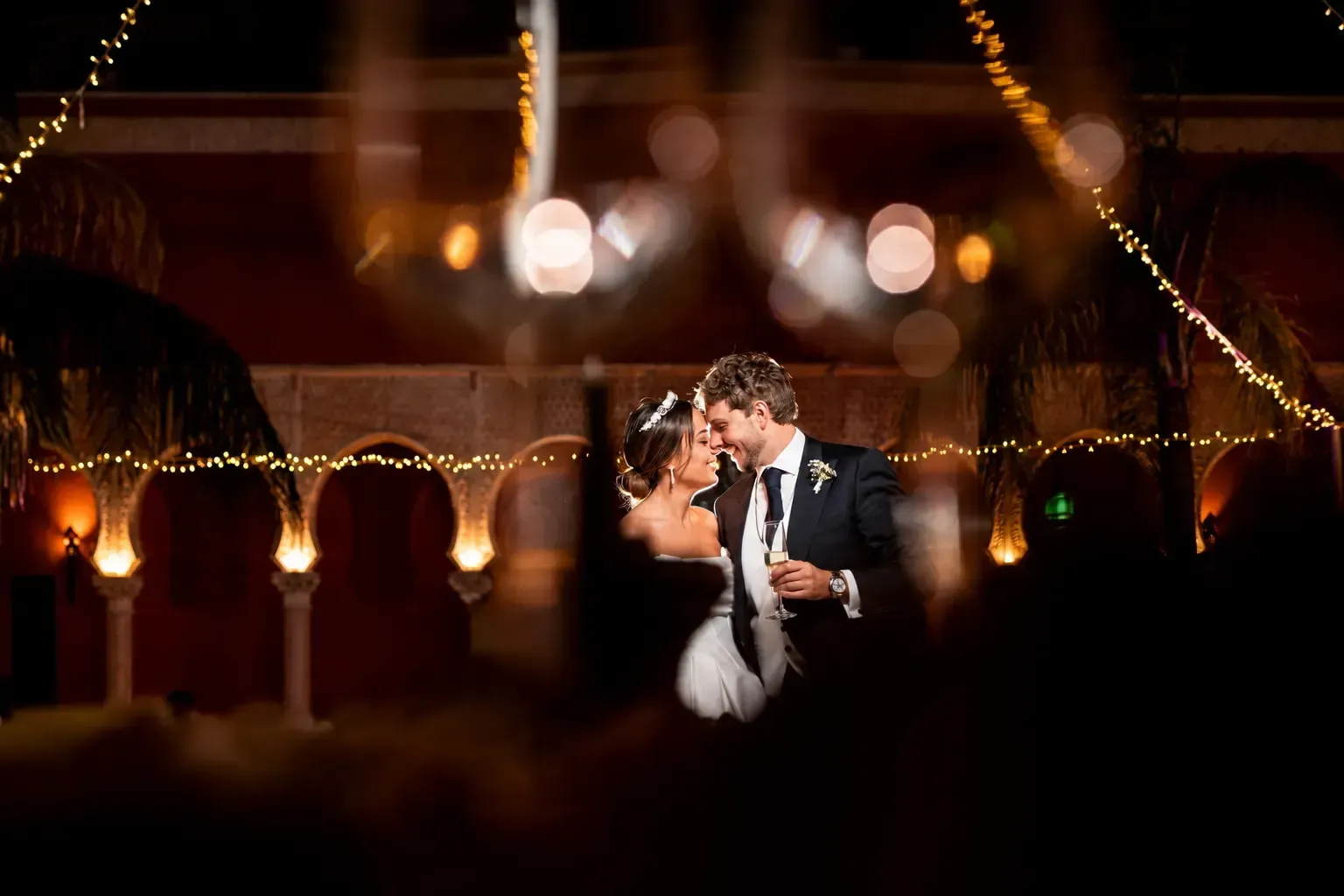 Novios besándose bajo cálidas luces de guirnalda en una recepción de boda nocturna.