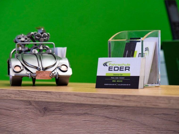 Eine Autoskulptur aus Metall neben einem Visitenkartenhalter auf einer Holzoberfläche vor grünem Hintergrund.