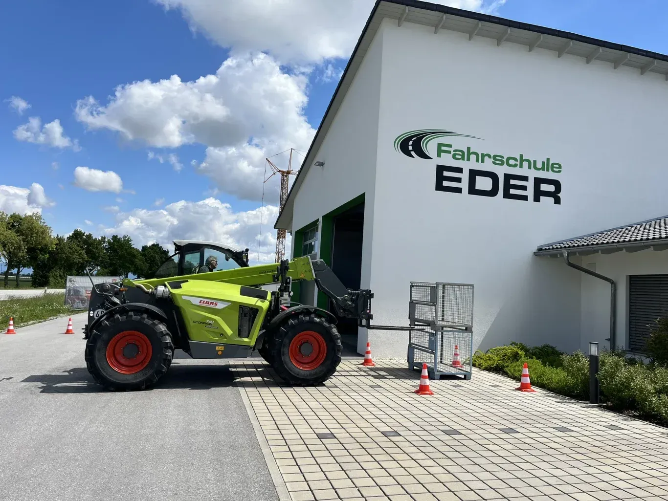 Ein grün-schwarzer Claas-Teleskoplader, geparkt vor einem Gebäude mit dem Schild „Fahrschule EDER“.