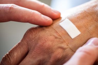Des mains qui tiennent délicatement une main recouverte d'un pansement adhésif blanc.