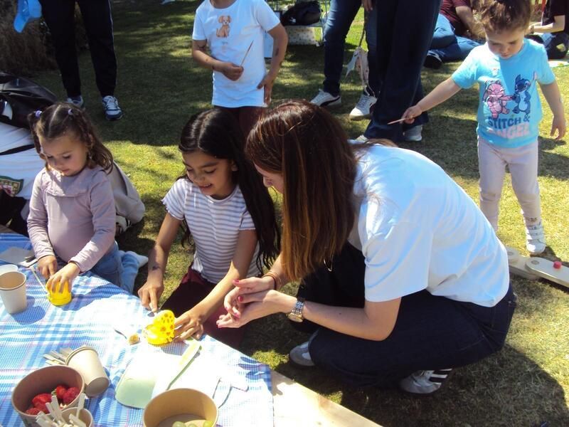 Una mujer está arrodillada ayudando a una niña con una manualidad.