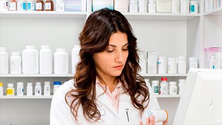 Una farmacéutica está mirando un frasco de medicamentos en una farmacia.