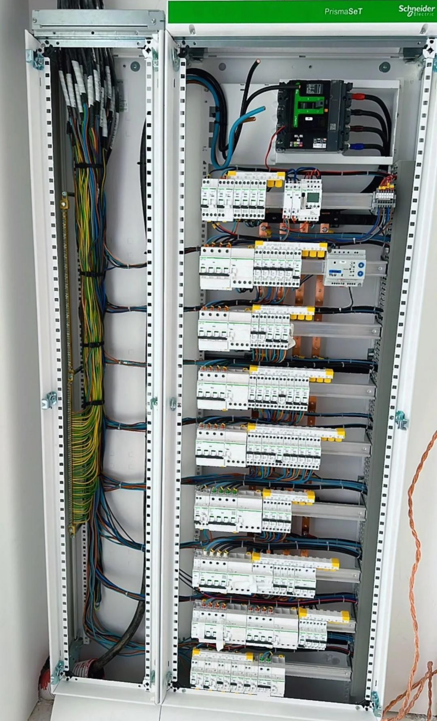 Boîte électrique couleur crème fixée sur un mur rose, avec des câbles noirs.