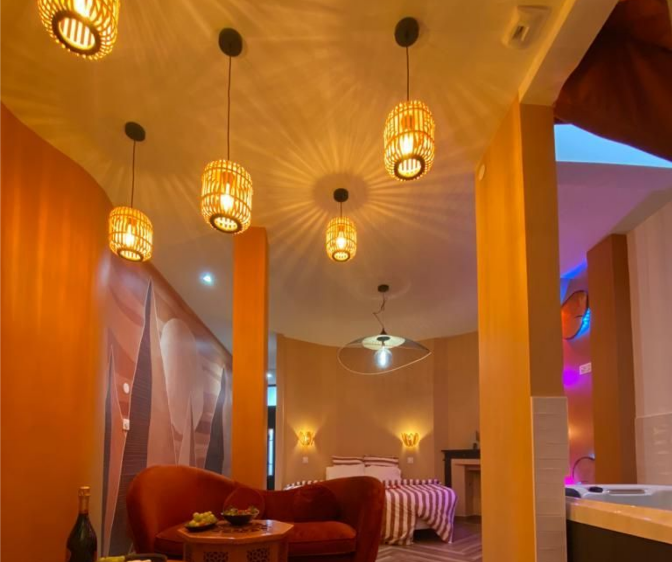 Chambre cosy éclairée par des suspensions décoratives. Murs orange, meubles rouge et lit en arrière-plan.