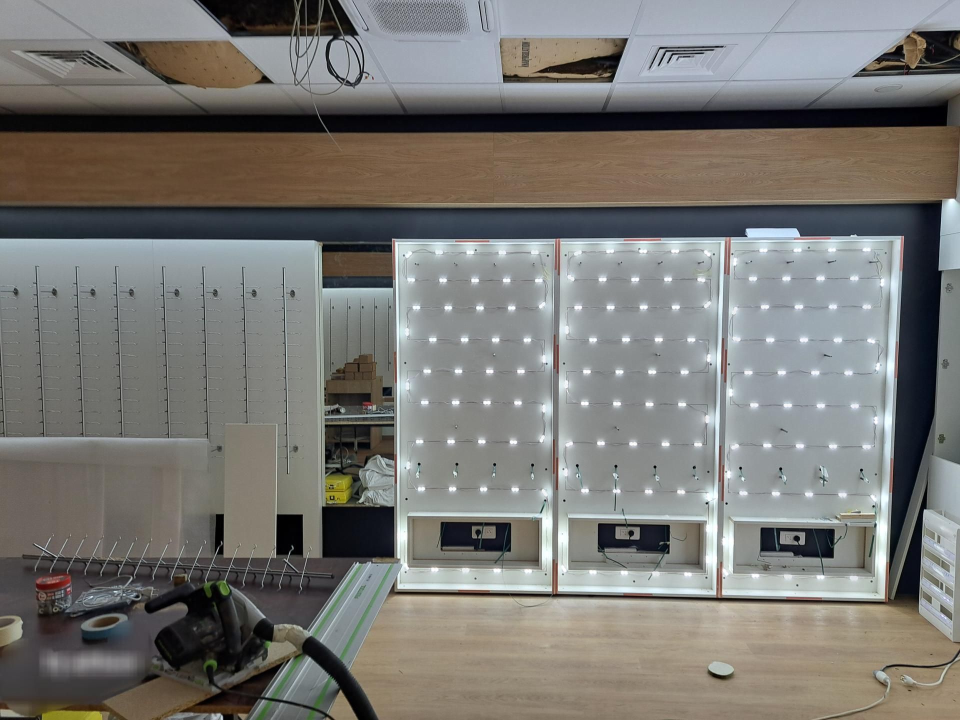 Espace intérieur en cours d'aménagement, comprenant trois panneaux d'affichage lumineux et des outils sur une table.