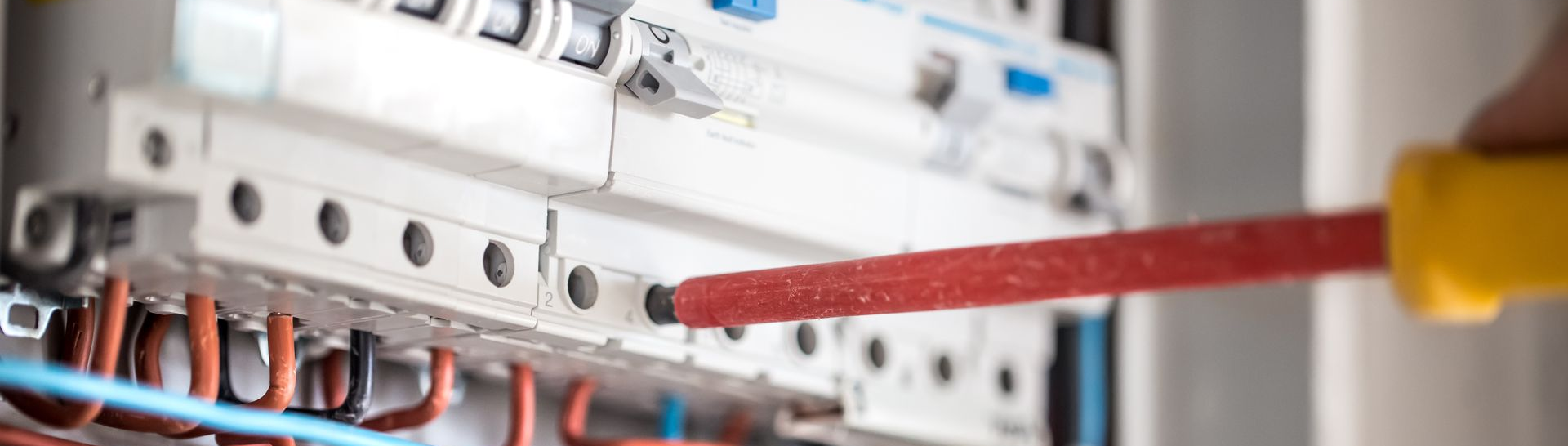 Une main utilisant un tournevis sur un panneau électrique.