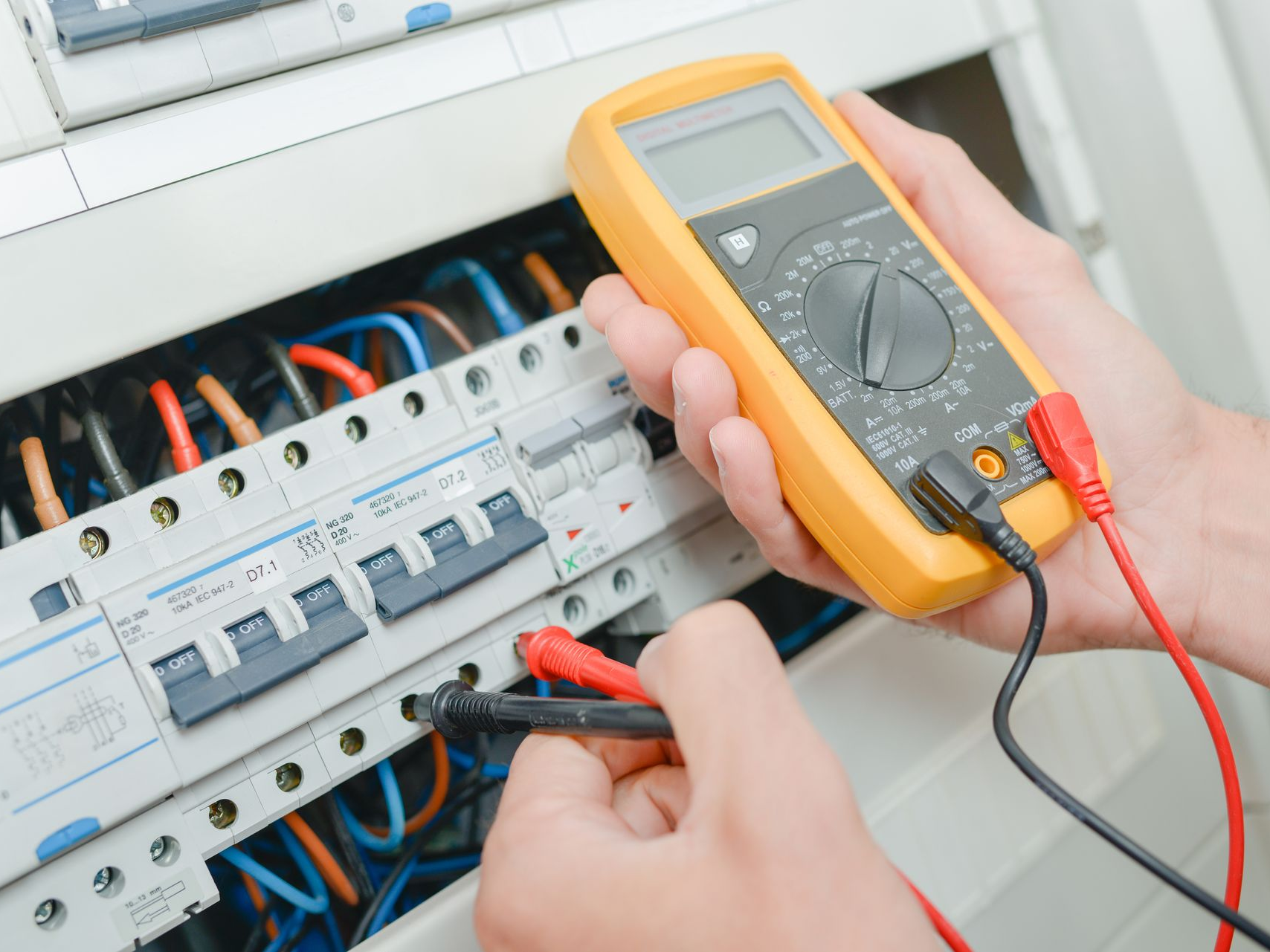 Une personne utilise un multimètre pour tester le câblage électrique d'un tableau électrique.
