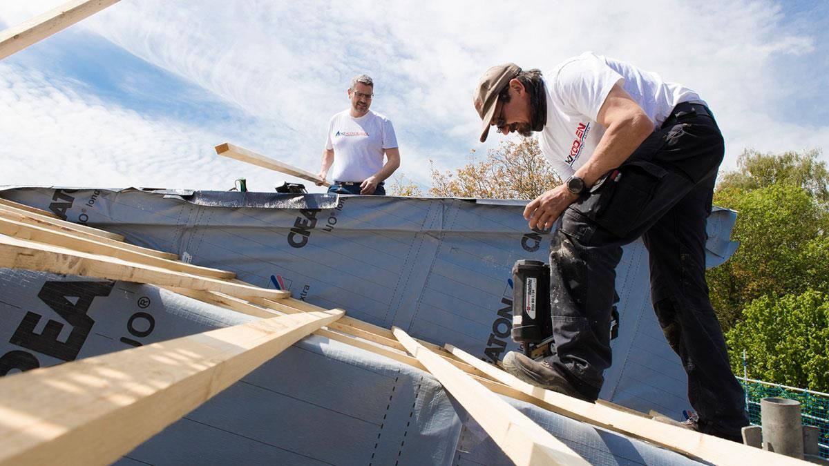 Zwei Männer arbeiten auf einem Dach und einer von ihnen trägt ein Hemd mit der Aufschrift „a“ darauf
