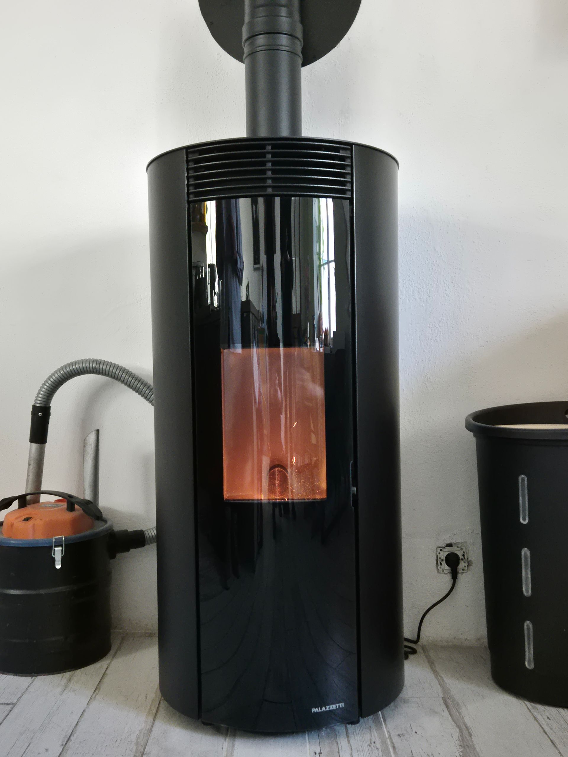 Poêle à granulés noir avec des flammes visibles dans une pièce, relié à un conduit d'évacuation.