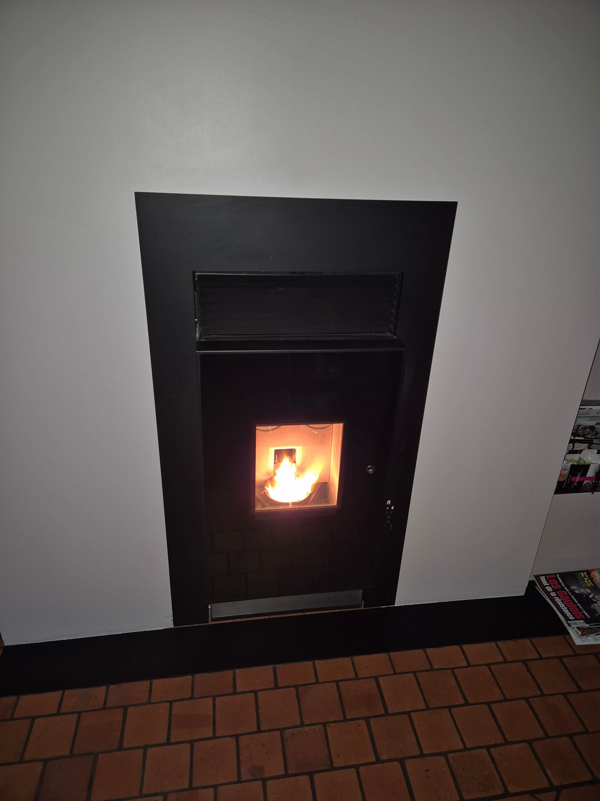 Cheminée murale noire avec un petit feu qui brûle dans une pièce intérieure.