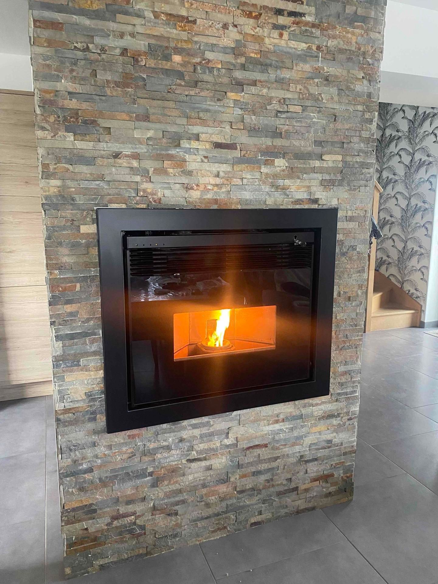Cheminée moderne noire avec un feu allumé encastré dans un mur en pierres sèches.