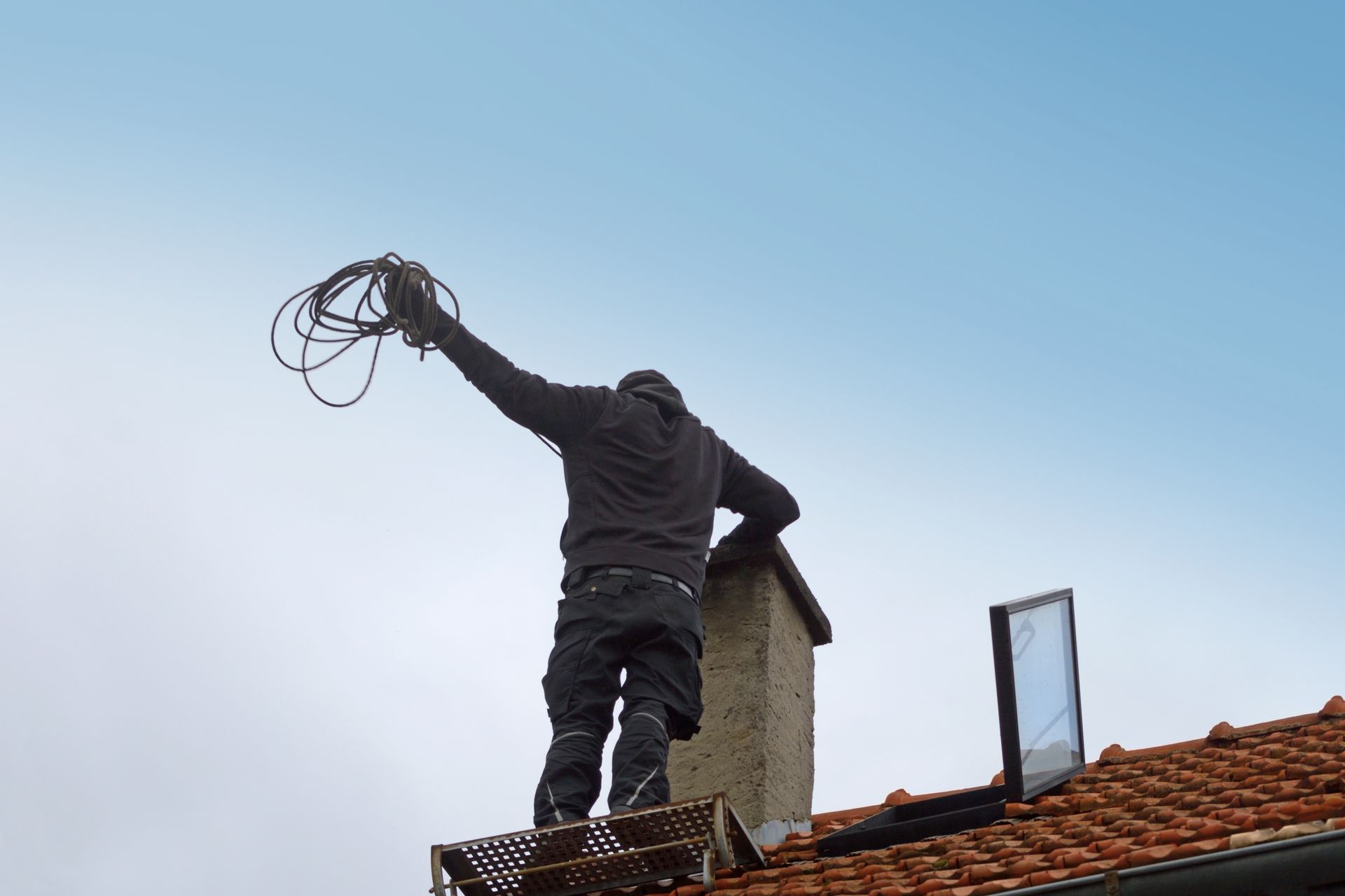 Une personne sur un toit tient un câble sur fond de ciel bleu.