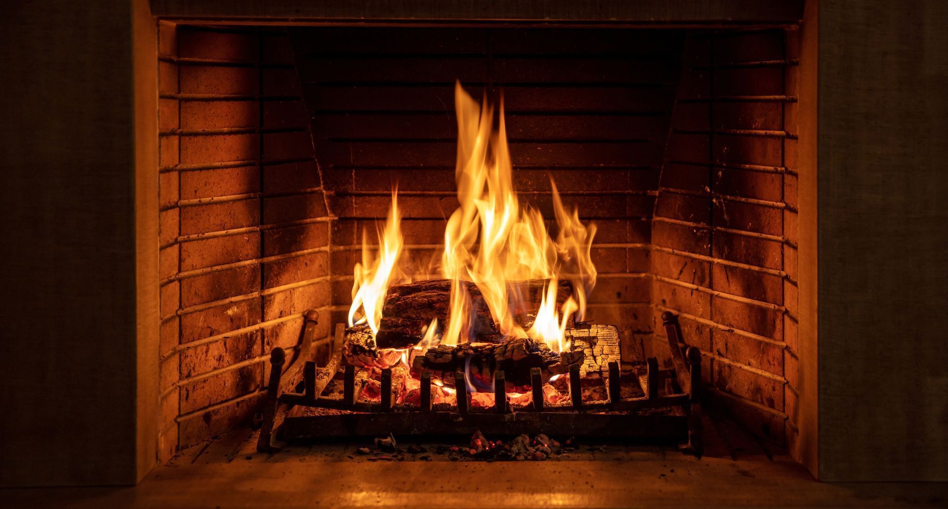 Une cheminée en briques allumée, avec des bûches incandescentes et de hautes flammes orange.