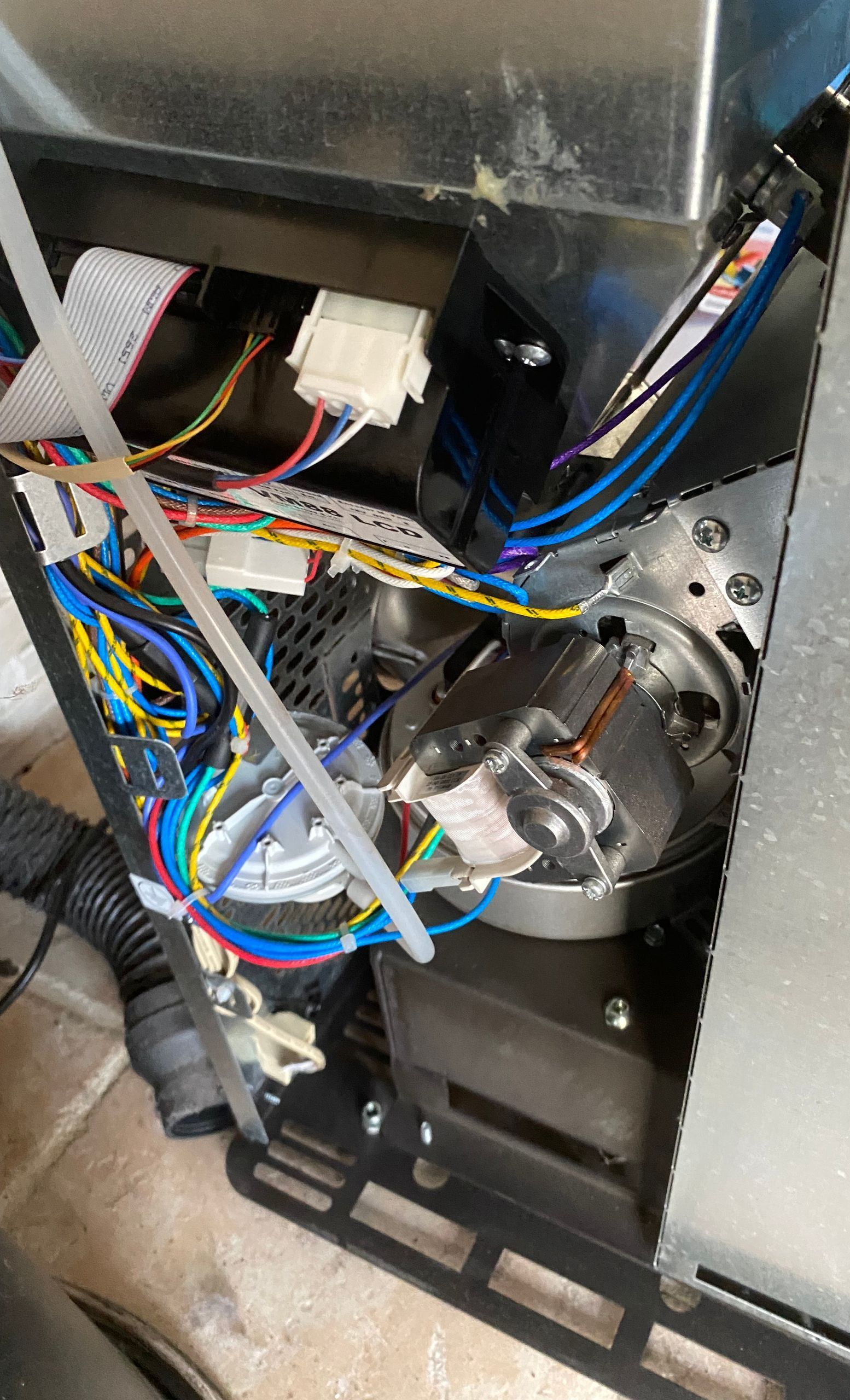 Panneau électronique ouvert avec des connecteurs et un ensemble moteur métallique à l'intérieur d'un poêle.