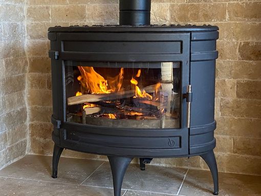 Poêle à bois noir avec un feu qui brûle à l'intérieur, adossé à un mur de briques.