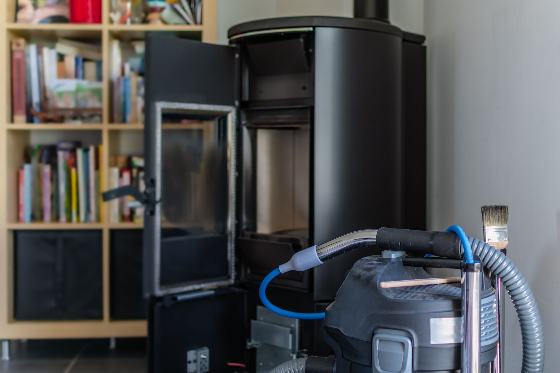 Aspirateur robot noir avec porte avant ouverte à côté d'un tuyau d'aspiration dans une pièce à vivre.