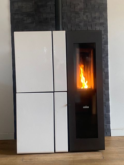 Poêle à granulés moderne blanc et noir avec flamme visible sur un mur carrelé foncé