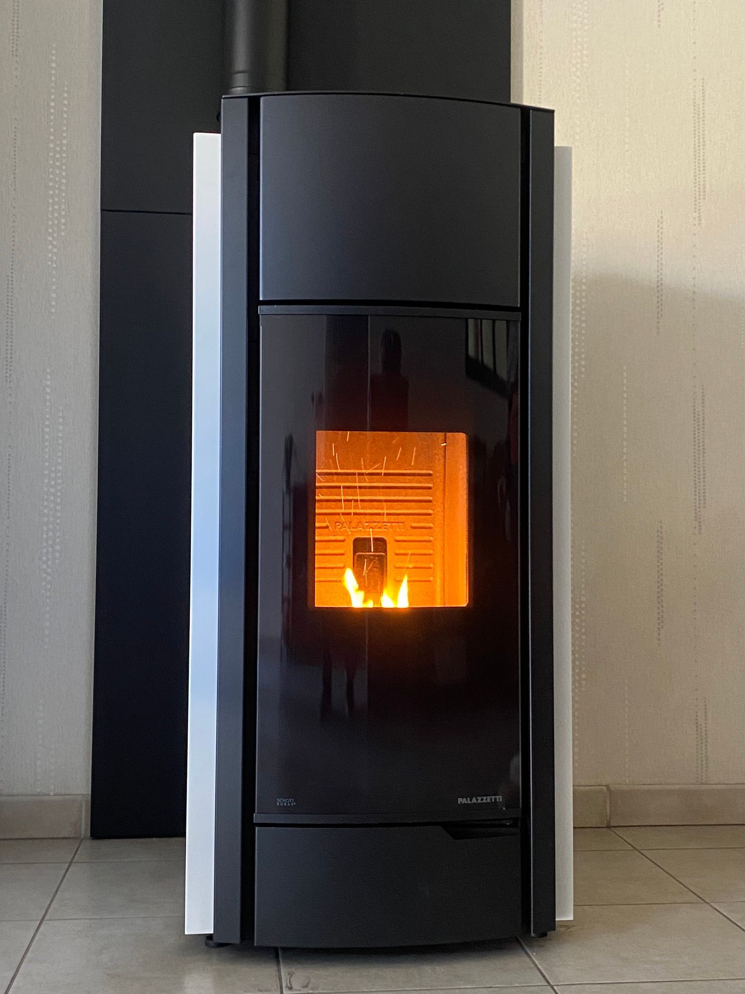 Poêle à granulés noir moderne avec un feu orange incandescent dans une pièce minimaliste.