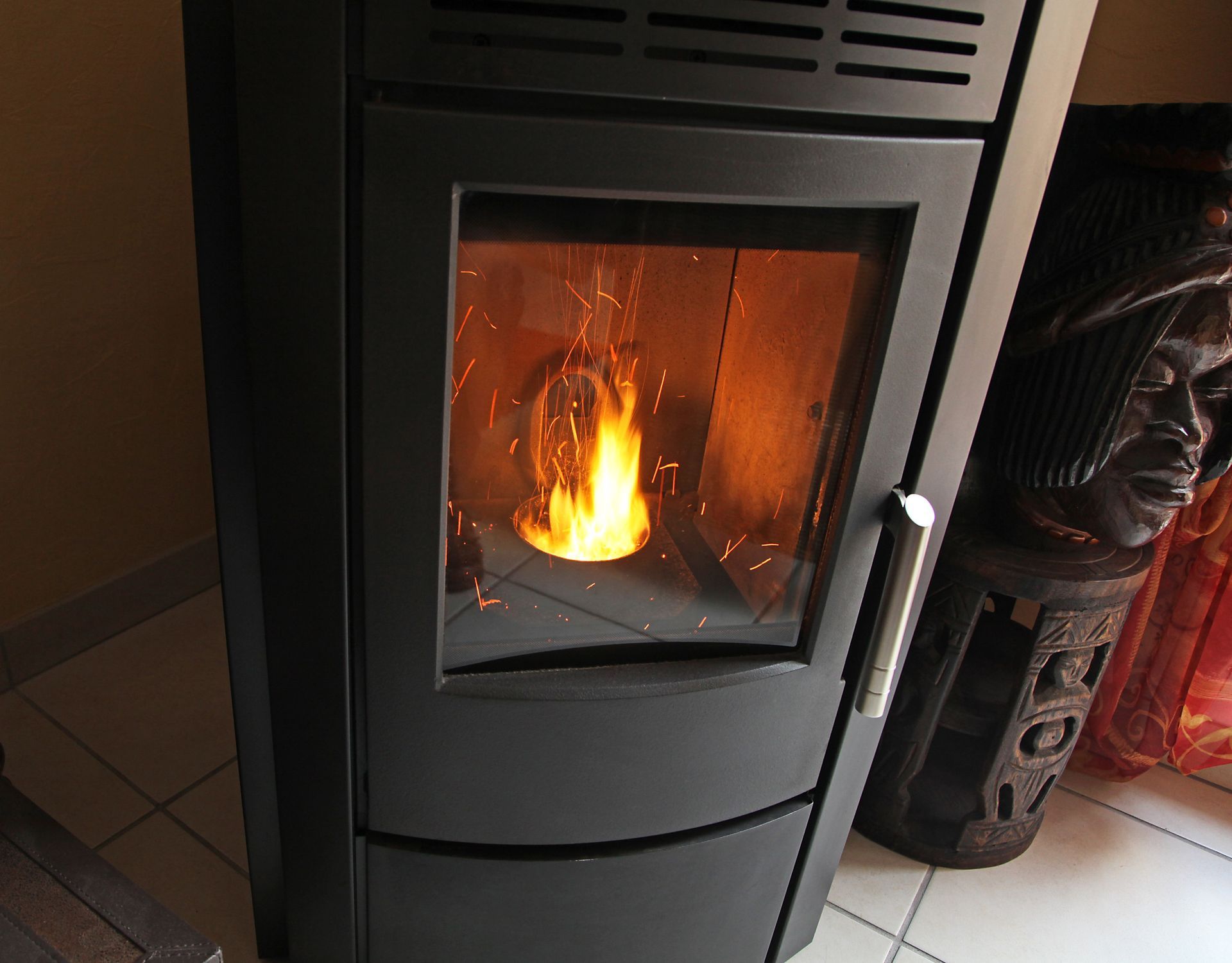 Poêle à bois noir avec un feu vif qui brûle derrière une porte vitrée.