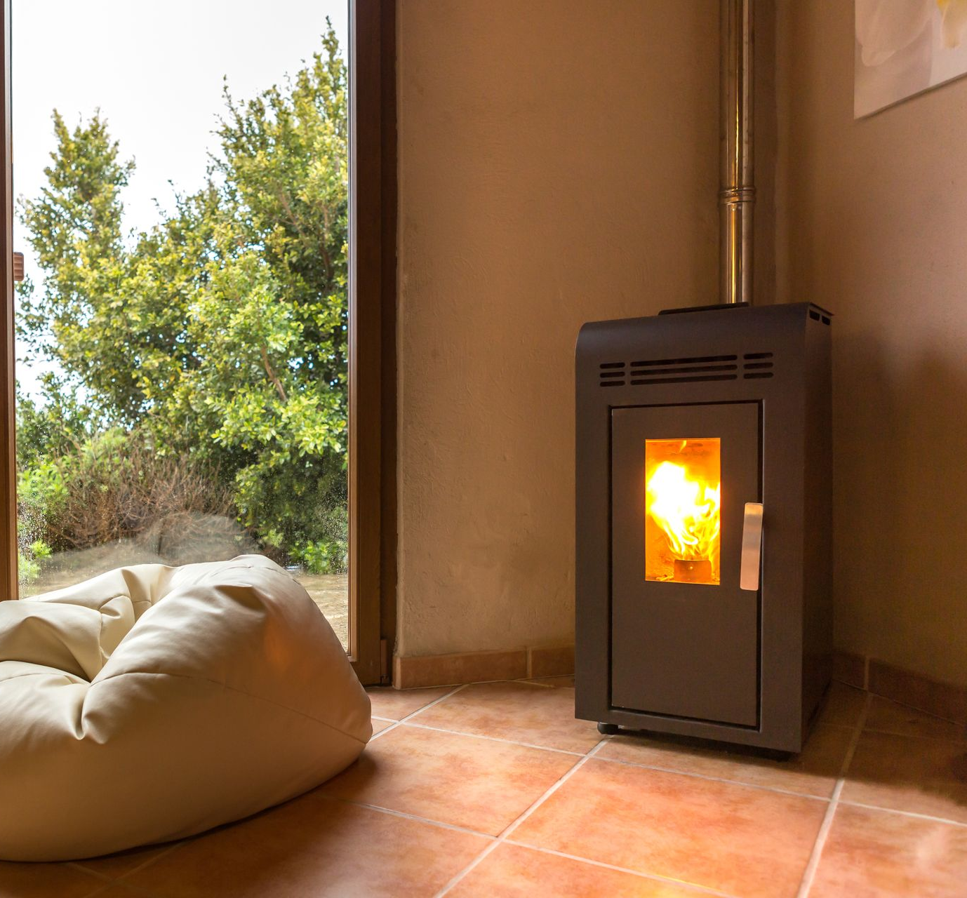 Une pièce confortable avec un poêle à granulés allumé près d'une fenêtre et un pouf sur des carreaux de terre cuite.
