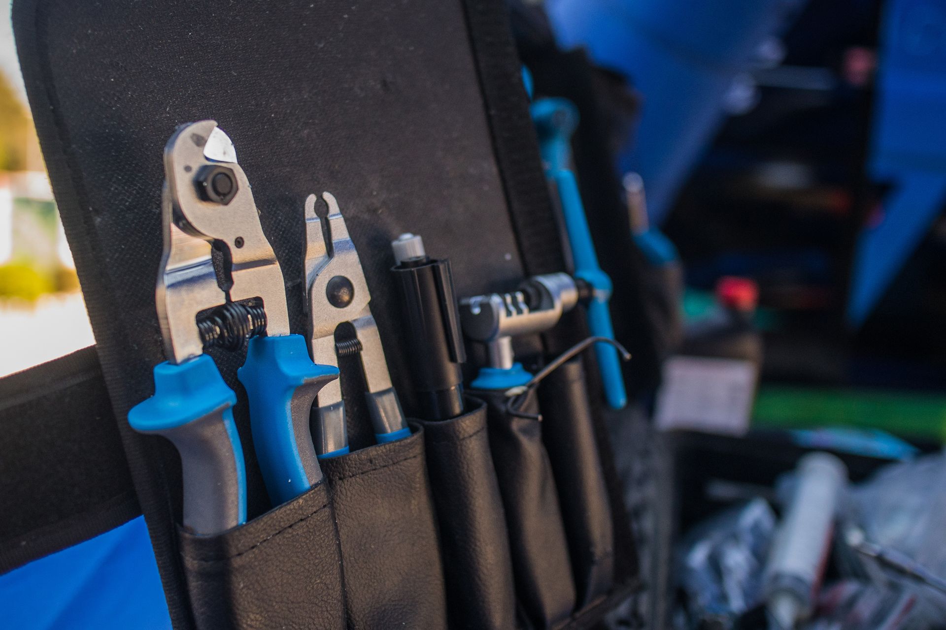 Des outils à main dans une trousse à outils noire, comprenant des pinces et des coupe-fils à poignées bleues, sur un établi.