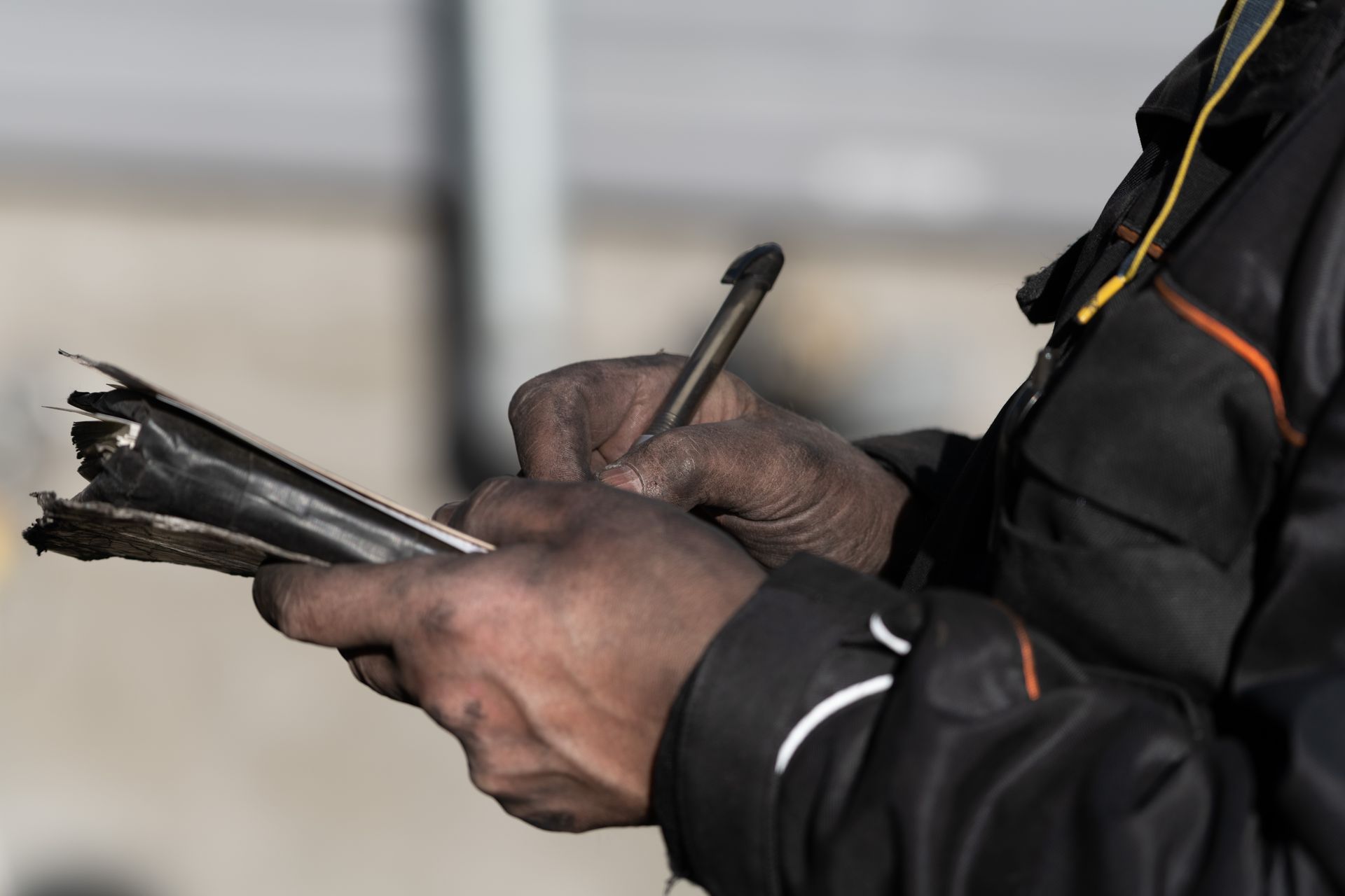 Des mains gantées de noir tiennent un carnet usé tandis qu'une personne écrit au stylo à l'extérieur.