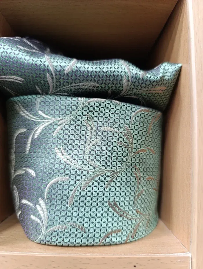 Conjunto de corbata y pañuelo de bolsillo color verde azulado en caja de madera, con estampado de enredaderas plateadas.