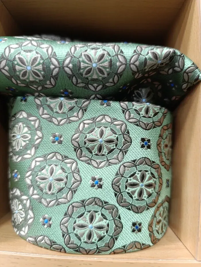 Corbata y pañuelo de bolsillo estampados en verde y gris en una caja de madera.