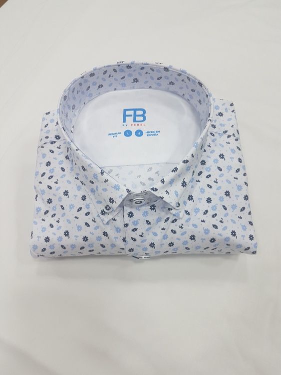 Camisa blanca doblada con estampado azul claro y gris oscuro, logo de la marca visible.
