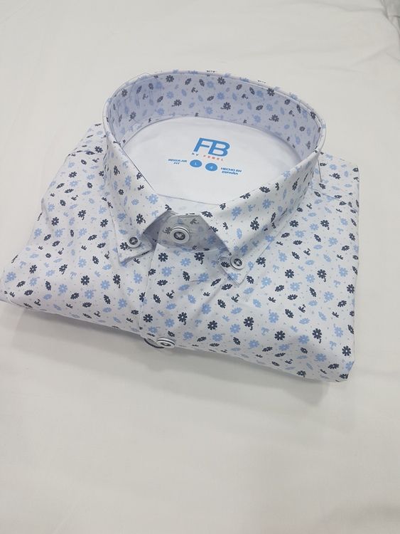 Camisa blanca abotonada con pequeño estampado floral azul, doblada cuidadosamente sobre una superficie blanca.
