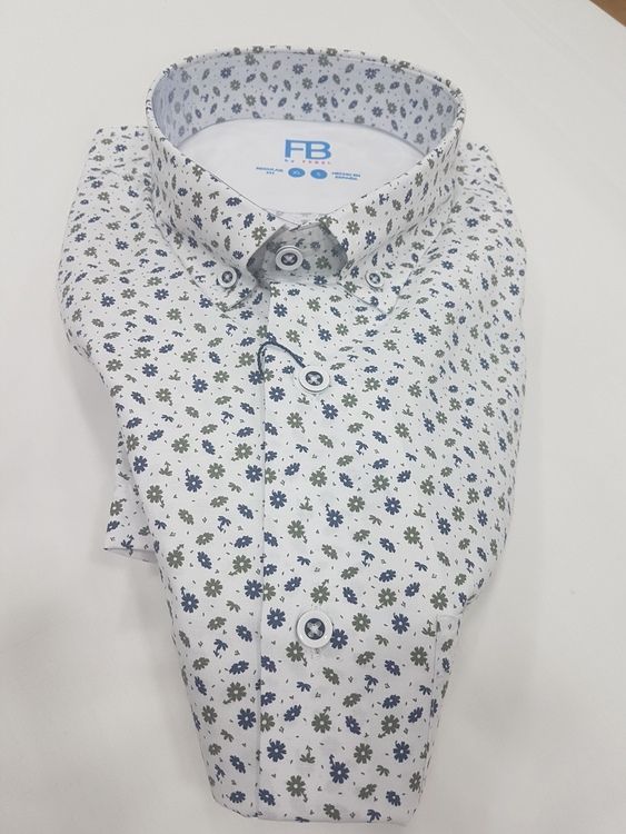 Camisa blanca con botones, con pequeño estampado floral azul y amarillo, doblada sobre una superficie blanca.
