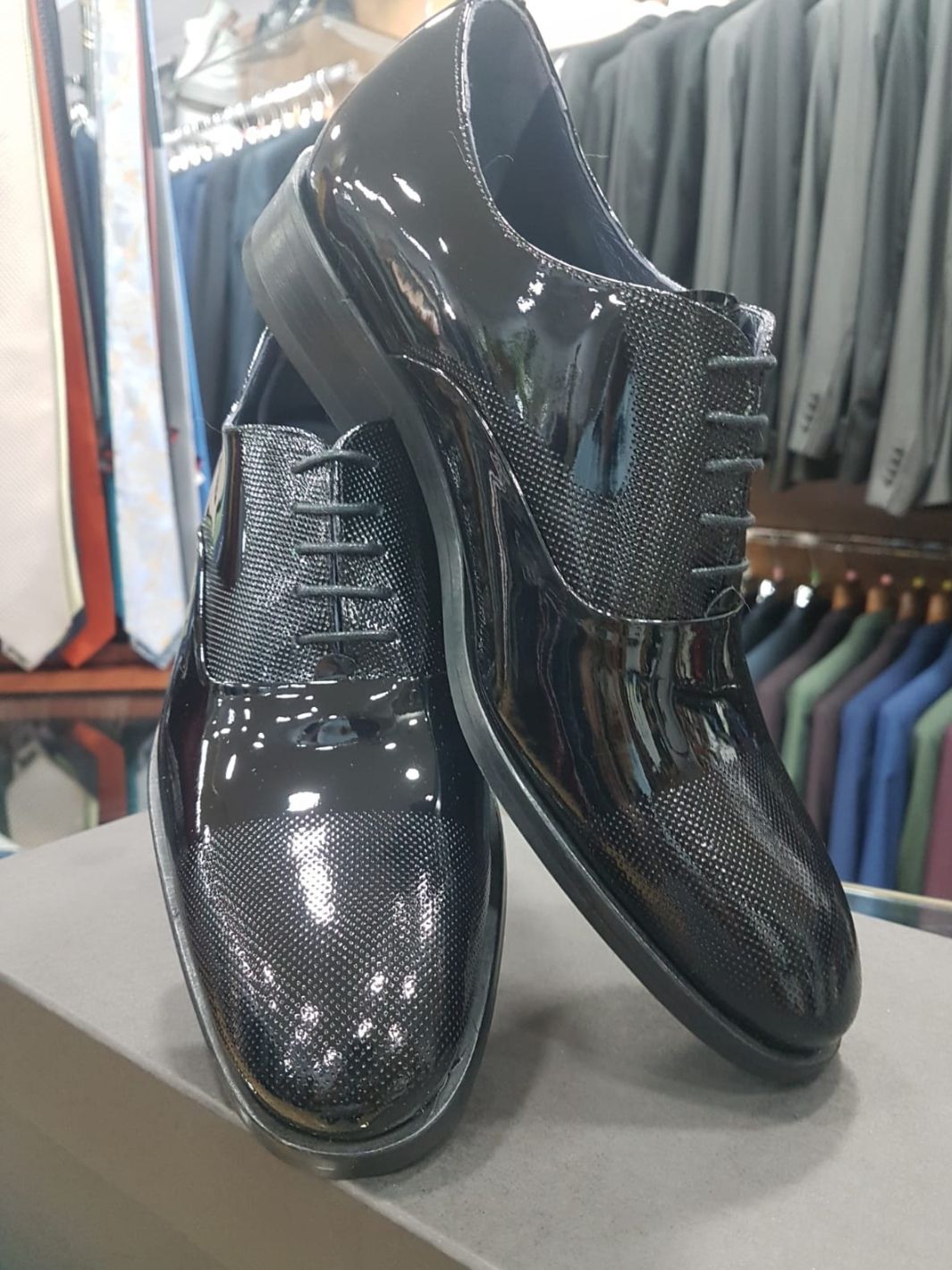 Zapatos de vestir de charol negro con detalles texturizados, expuestos en una tienda.