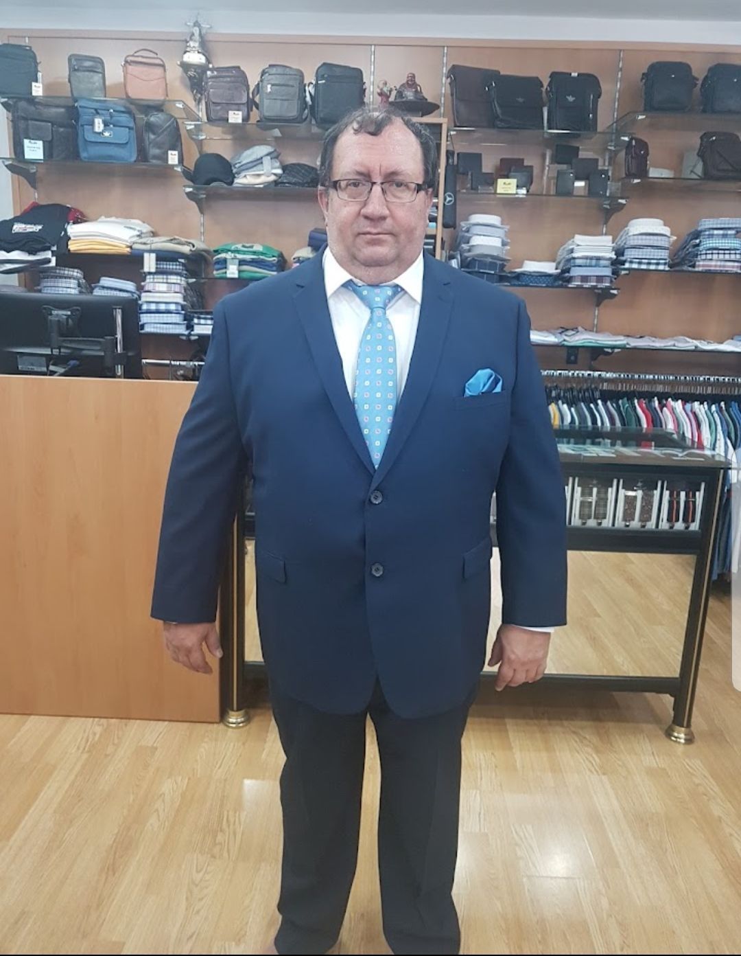 Hombre con traje azul y corbata, de pie en una tienda de ropa, sonriendo.