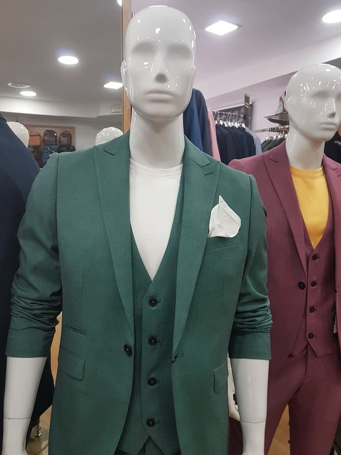 Maniquí con traje verde, camisa blanca y pañuelo de bolsillo. Otro maniquí con traje rojo. Interior de tienda.