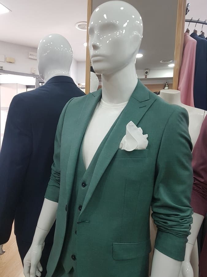 Maniquí con traje verde y pañuelo de bolsillo blanco en una tienda de ropa.