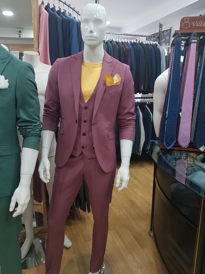 Maniquí con traje de tres piezas malva con camisa amarilla y pañuelo de bolsillo, en una tienda de ropa.