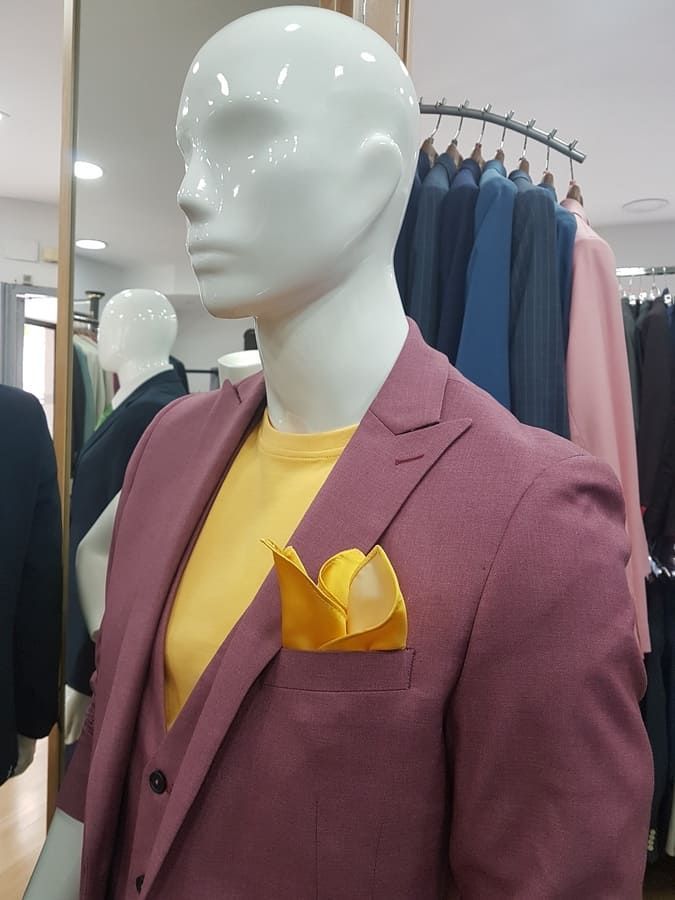 Maniquí con traje burdeos, camisa amarilla y pañuelo de bolsillo. Tienda con trajes en perchero.