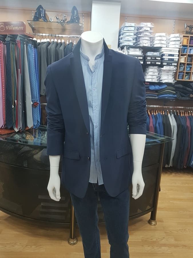 Maniquí con blazer azul marino, camisa azul claro y jeans, dentro de una tienda de ropa.